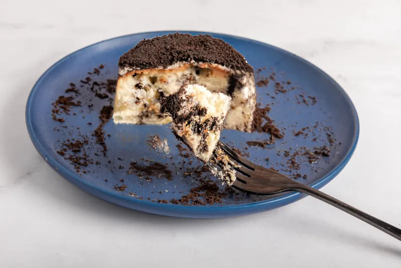 NY Oreo Cheesecake individual cortado en plato azul, con trozos de galleta en el relleno
