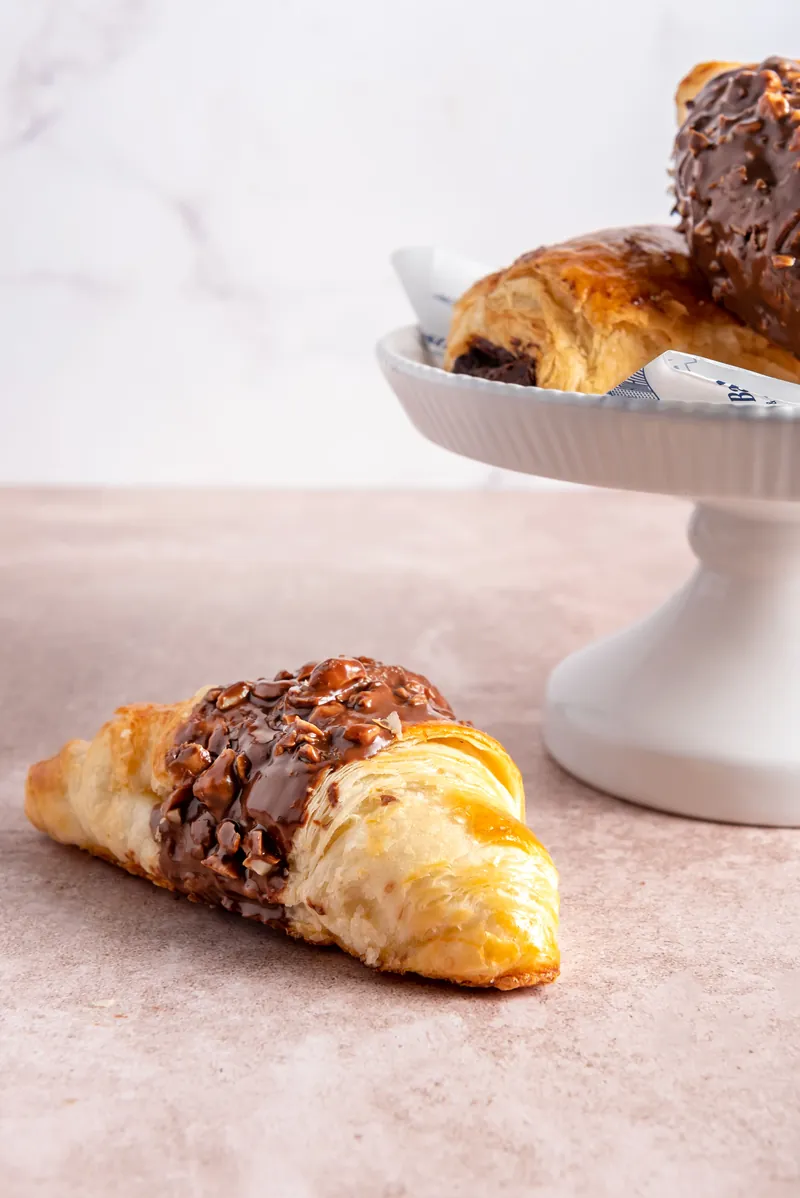 Chocolatín y croissant con chocolate en pedestal, con un croissant cubierto de chocolate y avellana